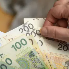Dłoń trzyma plik banknotów 100 i 200 zł, symbolizujący nową płacę minimalną.