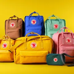En samling färgglada Fjällräven Kånken-ryggsäckar i olika fjällräven ryggsäck storlek, från små till stora, mot en gul bakgrund.