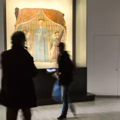 La Madonna del Parto di Piero della Francesca, con visitatori che la ammirano in un museo.