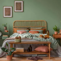 Gemütliches Schlafzimmer mit Rattan-Kopfteil, mintgrüner Bettwäsche und Korallen-Akzenten. Ein Holzbett mit Kissen und Decken lädt zum Entspannen ein. Pflanzen und Bilder runden das Ambiente ab, um das Bett perfekt einzurichten.