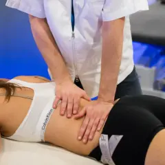 Un professionnel effectue un massage musculaire sportif sur le dos d'une femme allongée sur une table de massage.