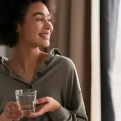 Une femme souriante tient un verre d'eau, un geste simple qui symbolise le luxe de l'eau de riche, une hydratation pure et précieuse.