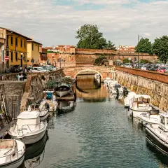 Boats docked along a canal in Livorno, Italy, with a brick bridge in the background.