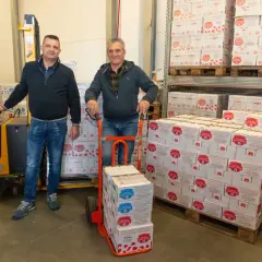 Due uomini in un magazzino con scatoloni di latte a lunga conservazione aperto fuori dal frigo.