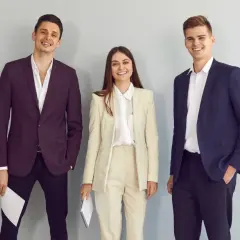 Trzy uśmiechnięte osoby w eleganckich strojach. Idealny przykład, co ubrać na rozmowę kwalifikacyjną.