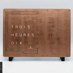 Horloge murale au design industriel, avec une plaque de cuivre gravée de lettres formant des mots. Une lettre métal unique pour un style épuré.