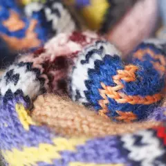 Gros plan sur un tissu jacquard aux motifs géométriques colorés, avec des fils de laine bleus, violets, jaunes et rouges entrelacés.
