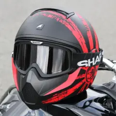 La calotta del casco Shark, nera con grafiche rosse a strisce e un sole nascente, è pronta per l'avventura.