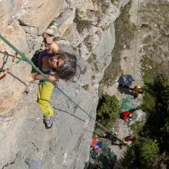 Frau klettert in Briançon, konzentriert sich auf den nächsten Griff. Unten warten Kletterer.