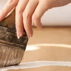 Main d'une personne peignant une surface en MDF avec un pinceau blanc.