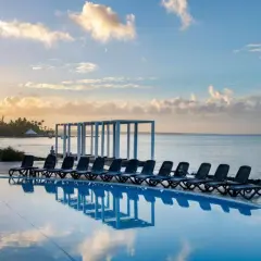 Słońce wschodzi nad Viva Dominicus Beach by Wyndham. Leżaki czekają nad basenem z widokiem na ocean i palmowe wybrzeże.