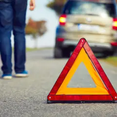 Triángulo de emergencia en carretera. Un hombre se acerca a un coche averiado, listo para proteger, avisar y socorrer.
