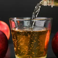 Apfelwein wird in ein Glas gegossen, umgeben von frischen Äpfeln. Ein gesunder Genuss!