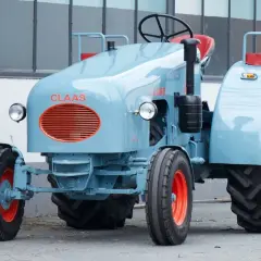 Niebieski ciągnik jednoosiowy Claas Jumbo z pomarańczowymi felgami i grillem.