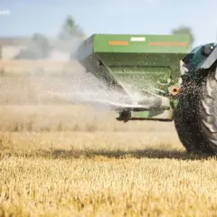 Traktor rozsiewa wapno magnezowe na polu. Drobinki nawozu unoszą się w powietrzu, poprawiając jakość gleby.