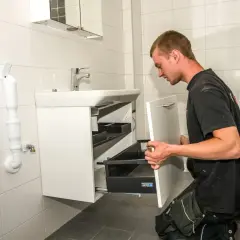 En man installerar en vit kommod i ett kaklat badrum.