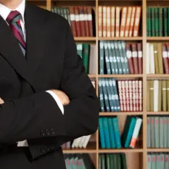 Prawnik w garniturze stoi przed regałami z książkami. Czy nakaz zapłaty jest wyrokiem? Odpowiedź znajdziesz w kodeksach.