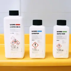 Three Ilford bottles for developing, stopping, and fixing film sit in a yellow tray, ready for creating the best black and white film.