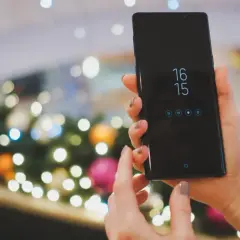 Ręce trzymające czarny smartfon Samsung, na ekranie zegar i ikony. Planowane zgranie kontaktów z Samsunga na komputer.