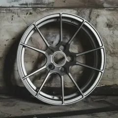 Nowoczesna felga aluminiowa 16 cali, z wieloma ramionami, prezentuje się na tle industrialnej ściany.