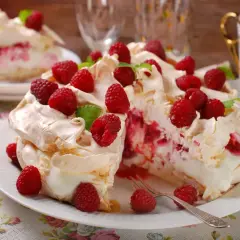 Pyszny tort bezowy z malinami, udekorowany świeżymi owocami i listkami mięty. Idealny na deser.