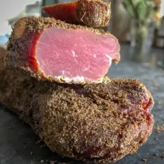 Un morceau de viande séchée, enrobé d'épices, dégage une odeur délicatement boucanée. Sa chair rose vif contraste avec sa croûte brune.