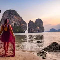 Kobieta w zwiewnej sukience spaceruje po plaży Ao Nang, podziwiając skaliste wysepki o zachodzie słońca.