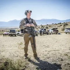 Mężczyzna w kamizelce taktycznej i spodniach Helikon Hybrid Tactical Pants trzyma karabin na strzelnicy.