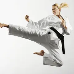 Kobieta w białym karate gi wykonuje wysokie kopnięcie w powietrzu.
