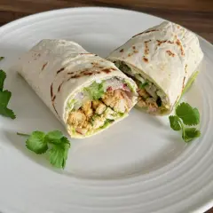 Kebab w tortilli przekrojony na pół, z kurczakiem, warzywami i ziołami, na białym talerzu.