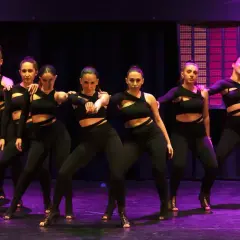 Un gruppo di ballerine in abiti neri si esibisce su un palco illuminato, creando un'atmosfera da dance hall.