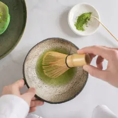 Hände bereiten Matcha zu, ein gesunder Genuss für die matcha schwangerschaft. Daneben grüne Pancakes mit Blaubeeren.