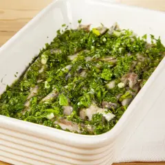 Acciughe al verde in una teglia bianca, condite con abbondante prezzemolo tritato e aglio.