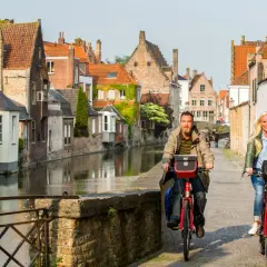 Couple enjoying a Bruges bike tour along a canal, with historic buildings lining the waterway.
