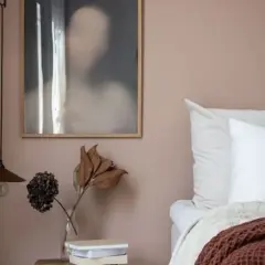 Un angolo letto con pareti color malva, un quadro astratto e un vaso con fiori secchi. Gli abbinamenti verde malva colore creano un'atmosfera rilassante.