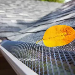 A yellow leaf rests on a newly installed gutter guard, showcasing its effectiveness against falling debris.