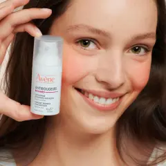 Ein lächelndes Gesicht hält eine Flasche Avène Antirougeurs. Ideal bei Rötungen, auch bei Neurodermitis.