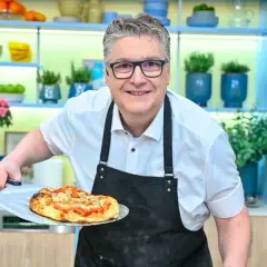 Uśmiechnięty kucharz prezentuje pyszną pizzę rzymską prosto z pieca.