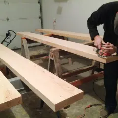 Man sanding Douglas fir planks on sawhorses, preparing them for staining.