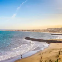 En vidsträckt gran canaria strand med turkost vatten, gyllene sand och några få besökare som njuter av solen.
