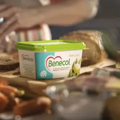 Pudełko margaryny Benecol na desce z warzywami i pieczywem.