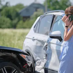 Kobieta rozmawia przez telefon obok dwóch uszkodzonych samochodów po kolizji.