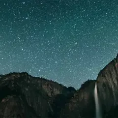 Nocne niebo pełne gwiazd nad wodospadem i górami. To niesamowite zdjecie kosmosu.