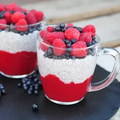 Dwa kubki pysznego chia pudding z malinami i borówkami, na tle drewnianych desek.