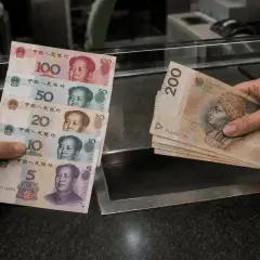 Ręka trzyma stos banknotów chińskiej waluty: 100, 50, 20, 10 i 5 juanów. Druga ręka podaje polskie banknoty 200 złotych.