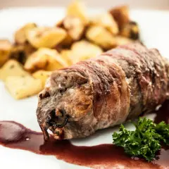 Zrazy z karkówki zawinięte w boczek, podane z pieczonymi ziemniakami i sosem.