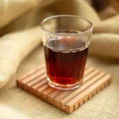 Ein Glas roter Rooibos Tee, perfekt für die Stillzeit, steht auf einem Holzuntersetzer.