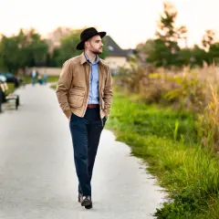 Mężczyzna w czarnym kapeluszu, jeden z wielu męskie nakrycia głowy rodzaje, spaceruje ścieżką wśród zieleni.