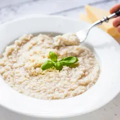 Kremowe risotto z parmezanem i bazylią na białym talerzu, widok z góry.