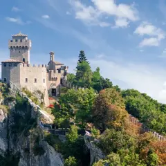 Trzy wieże San Marino na skalistym szczycie, otoczone zielenią. Widok na doliny, gdzie mieszka san marino ludność.